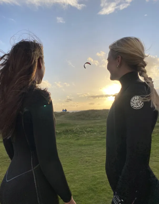 Two surfers looking out over the sea at sunset